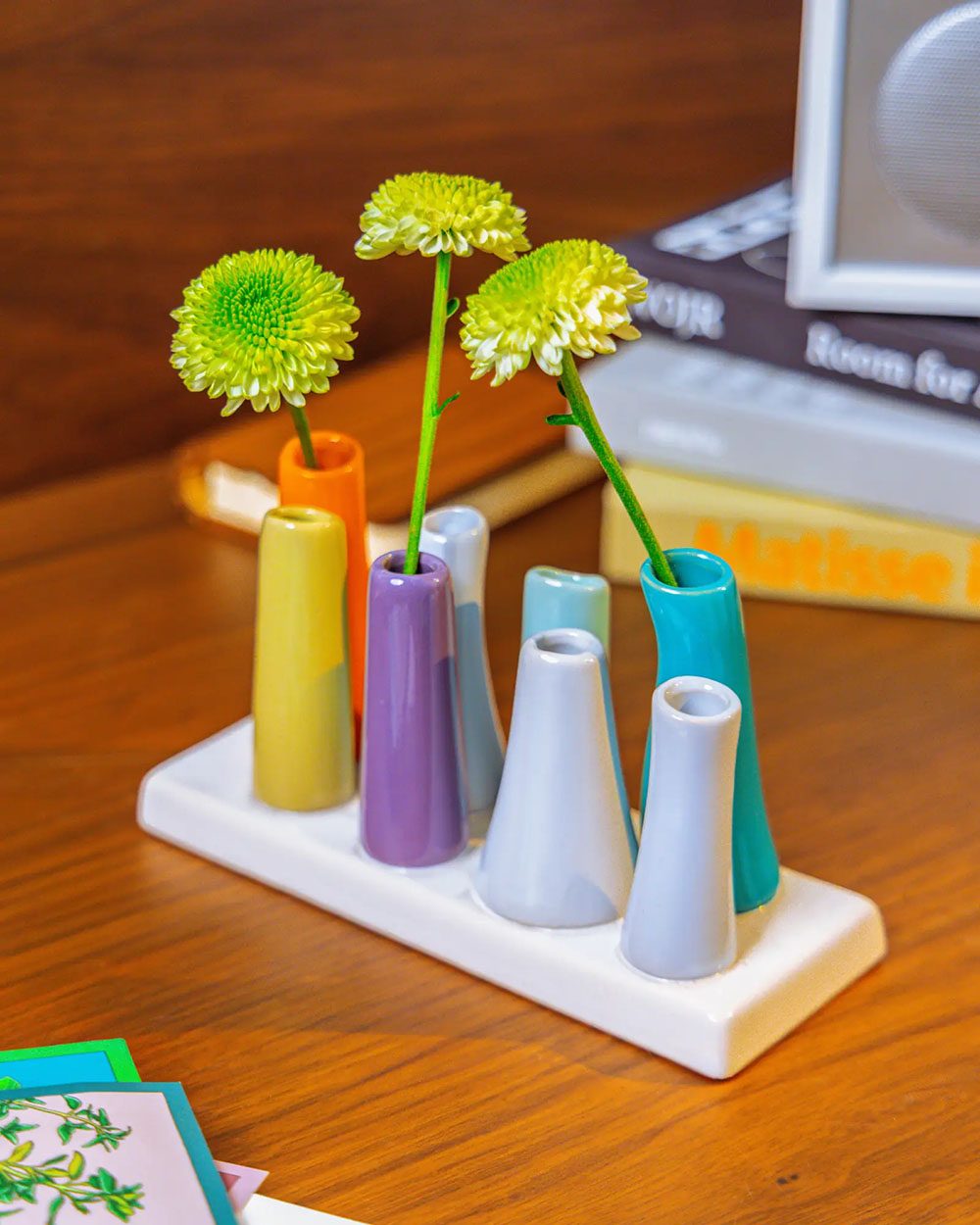 Chive ceramic pooley bud vase in colour orange, styled with fresh flowers, on a wood desk.